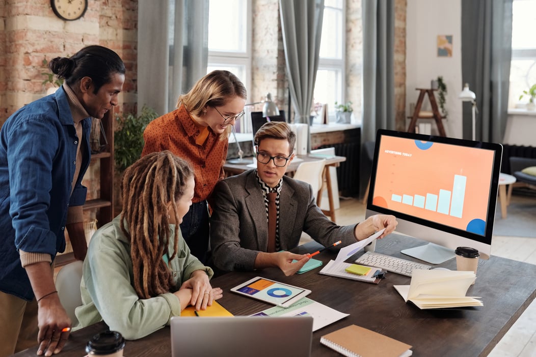 A Group of People Discussing Beside a Desktop with Graph on Screen